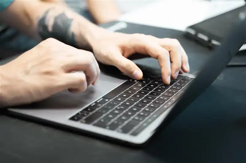 Eine Person arbeitet an einem Laptop, zu sehen sind nur die Hände, die das Mousepad nutzen und etwas auf der Tastatur eingeben