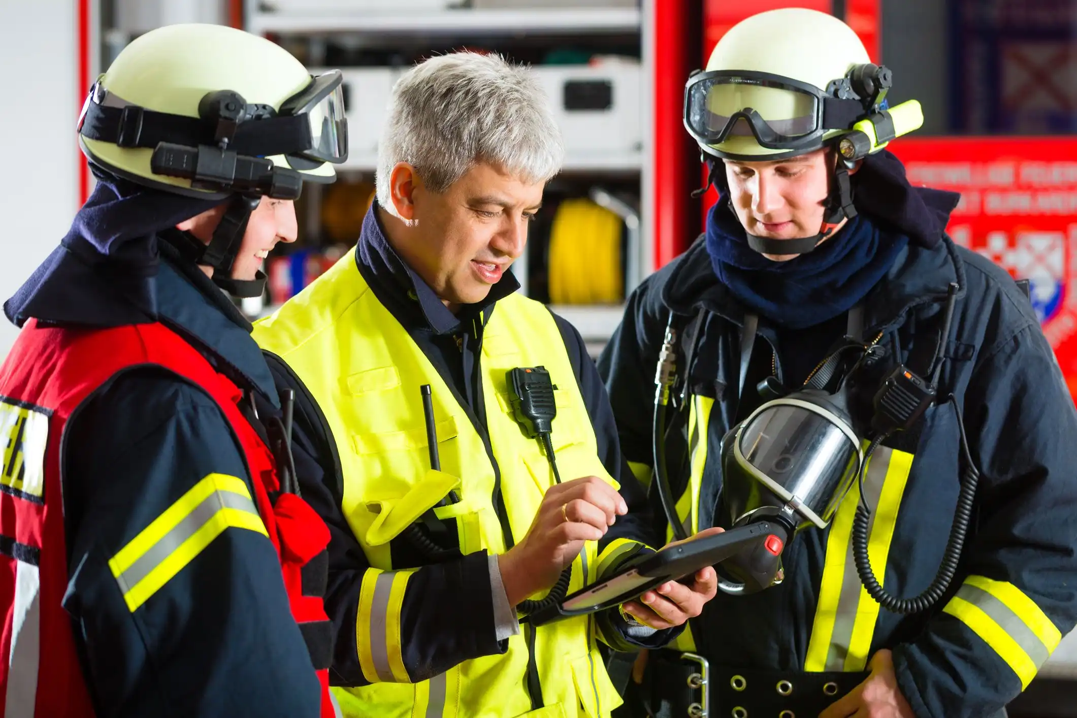 Ein Feuerwehroberkommandant erläutert zwei Feuerwehrleuten Einsatzinformationen auf einem Tablet
