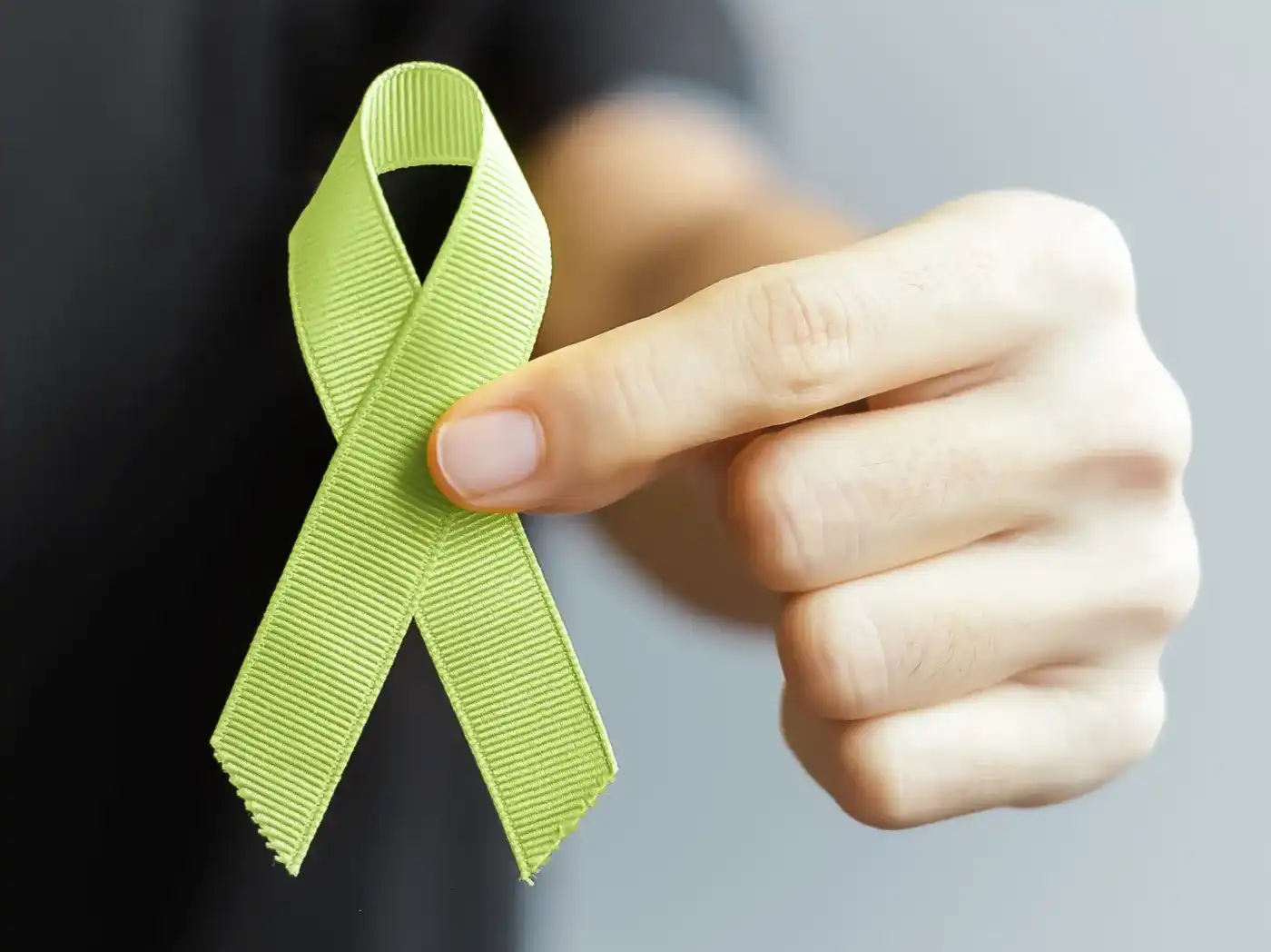 Eine grüne Schleife wird in die Kamera gehalten, diese wird von einer Person in der Hand getragen