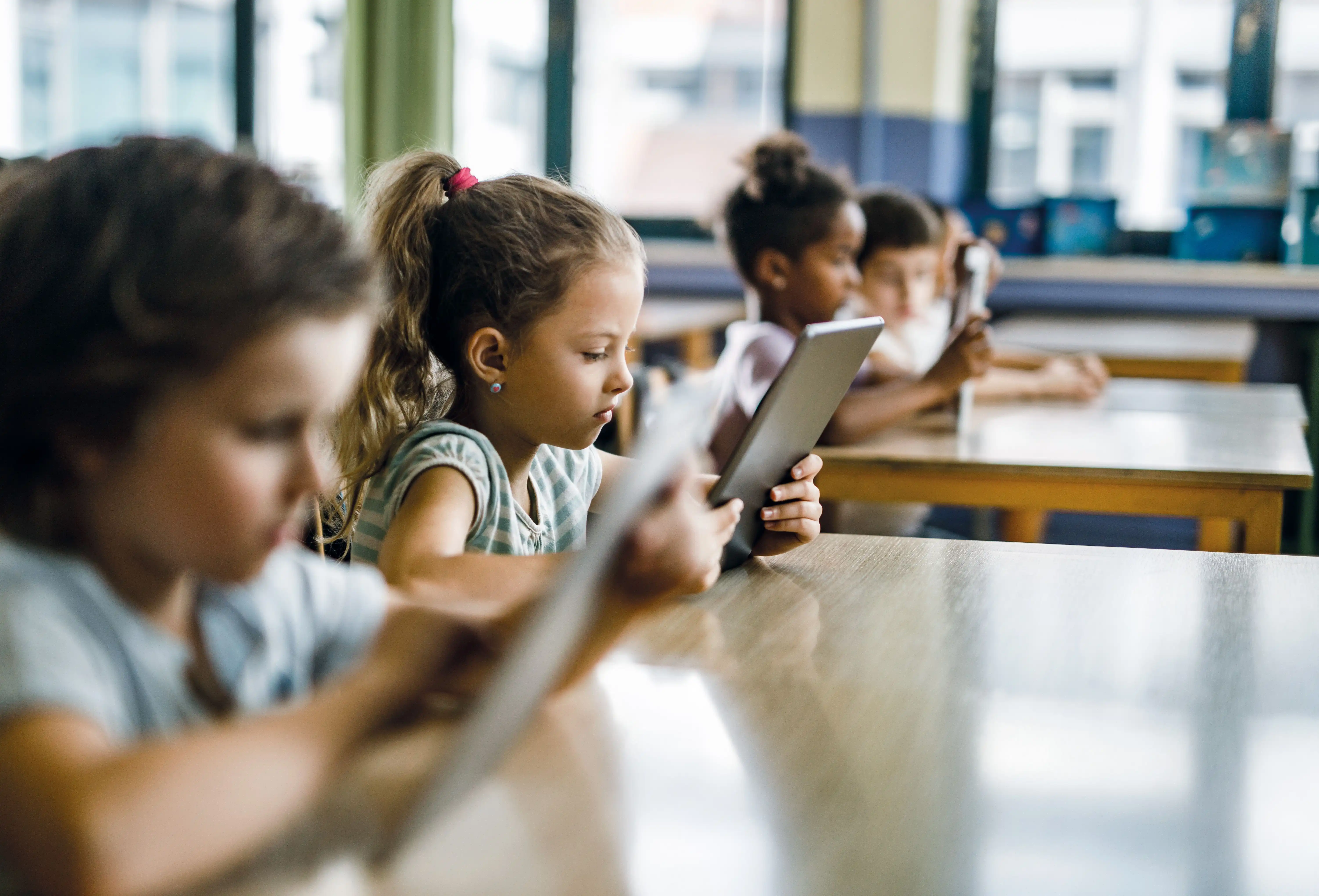 Jüngere Kinder in einem Klassenzimmer, alle haben jeweils ein Tablet in der Hand