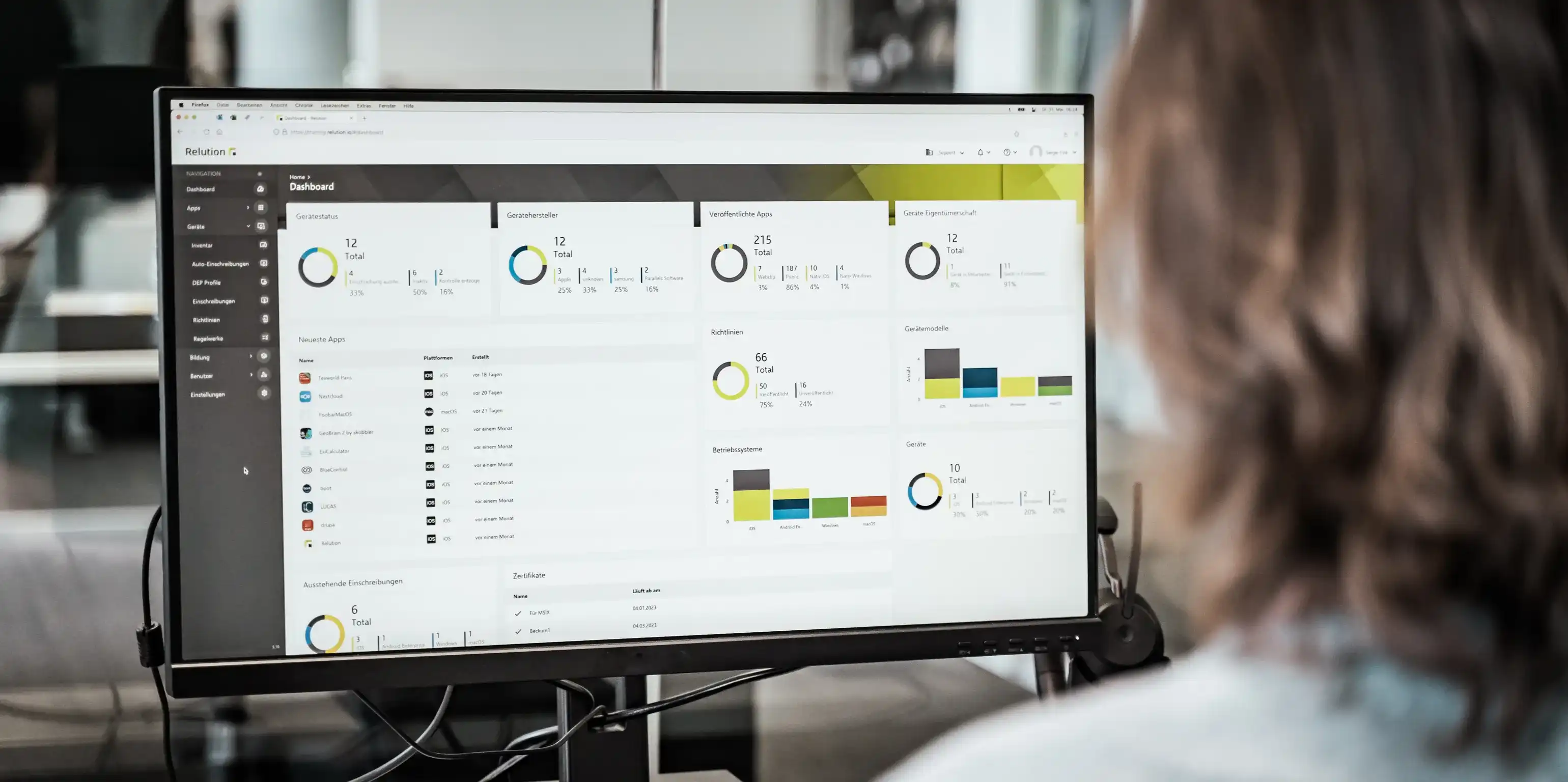 Eine Person sitzt vor einem großen Bildschirm, auf welchem verschiedene Diagramme und Zahlen sichtbar sind, die dem Relution-Dashboard zugeordnet sind