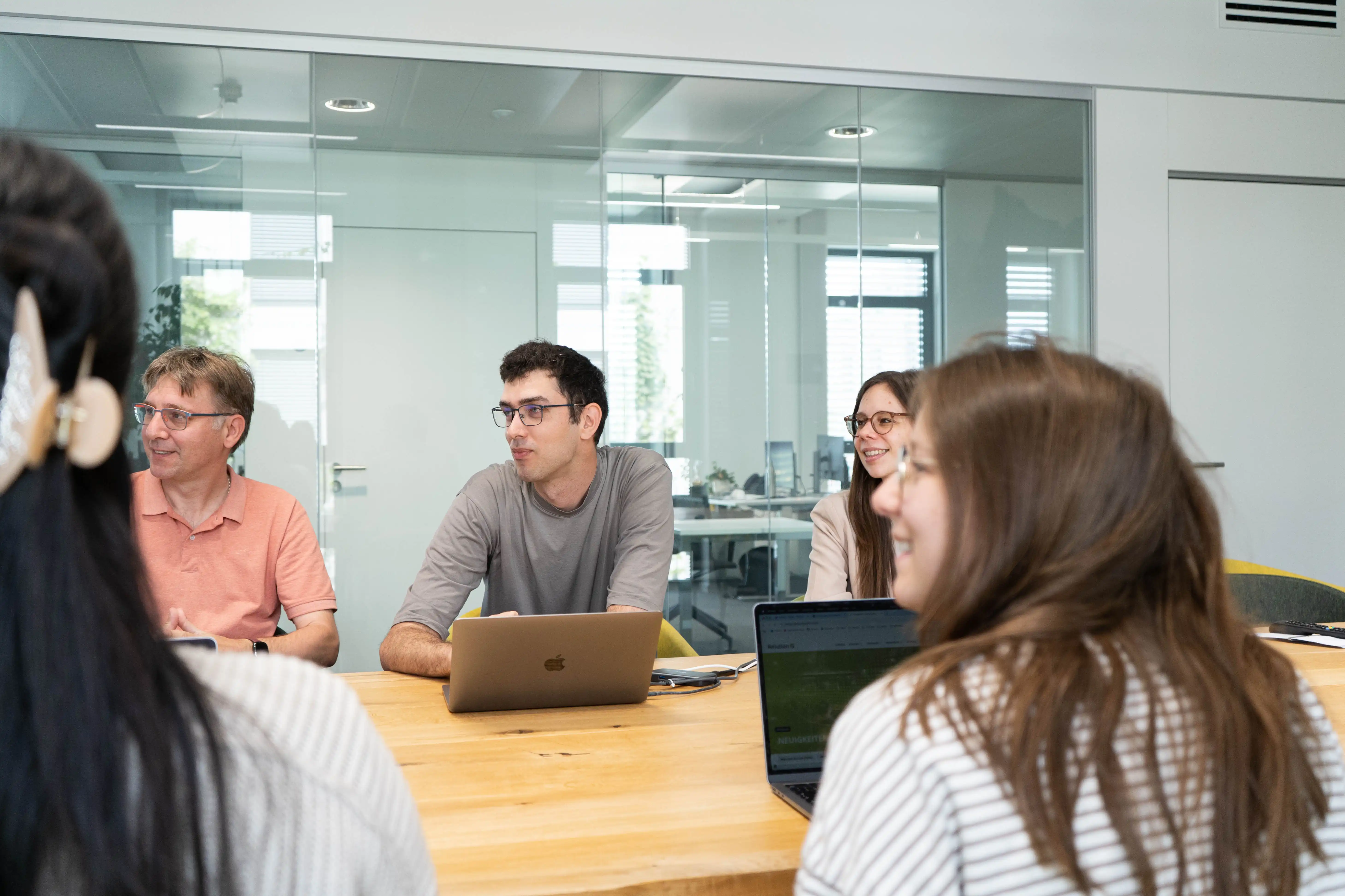 Mehrere Personen sitzen in einem modernen Meetingraum vor ihren Laptops und schauen aufmerksam in eine Richtung