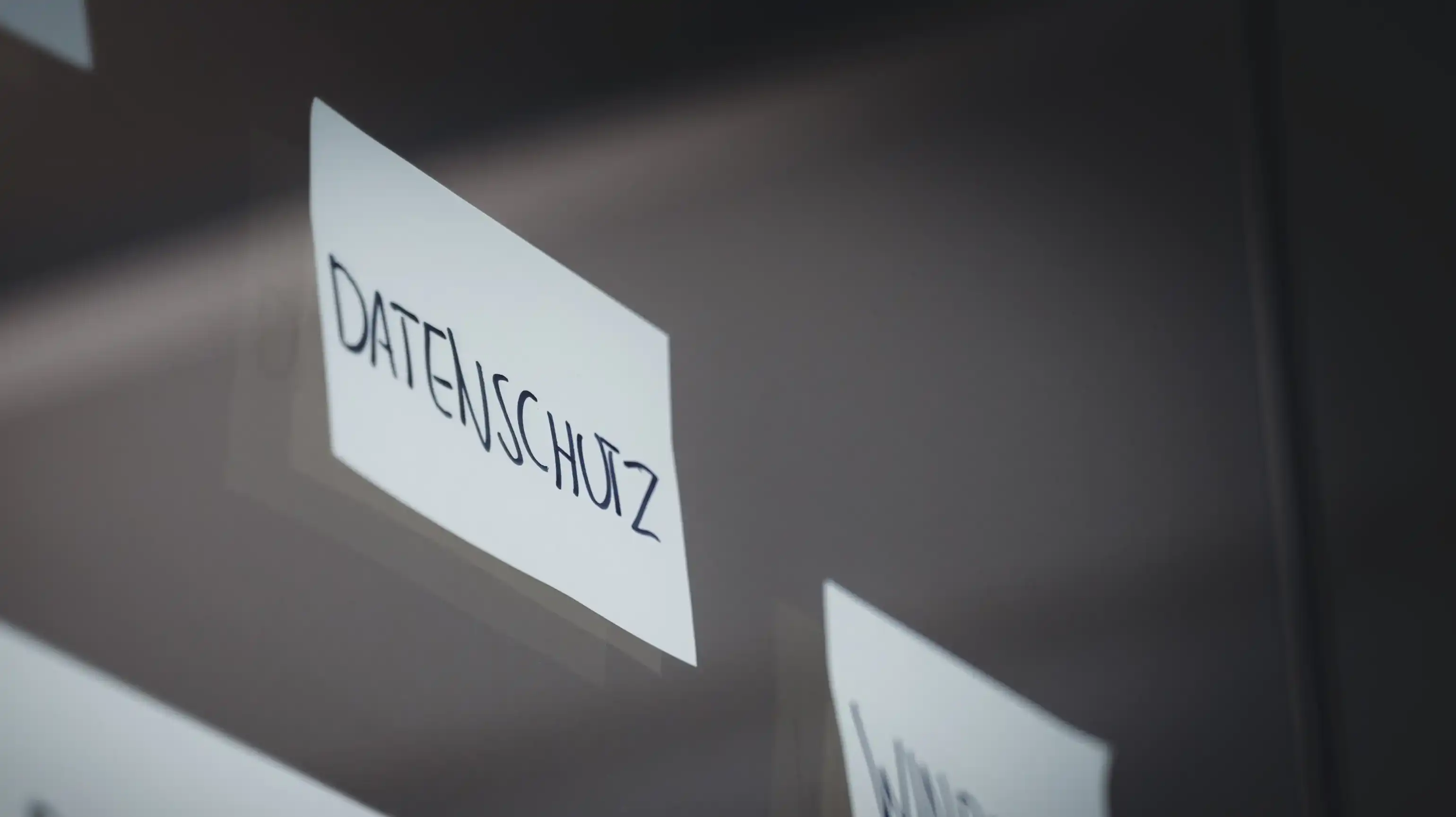 A Post-it is stuck to a glass pane, with the word "Datenschutz" written on it