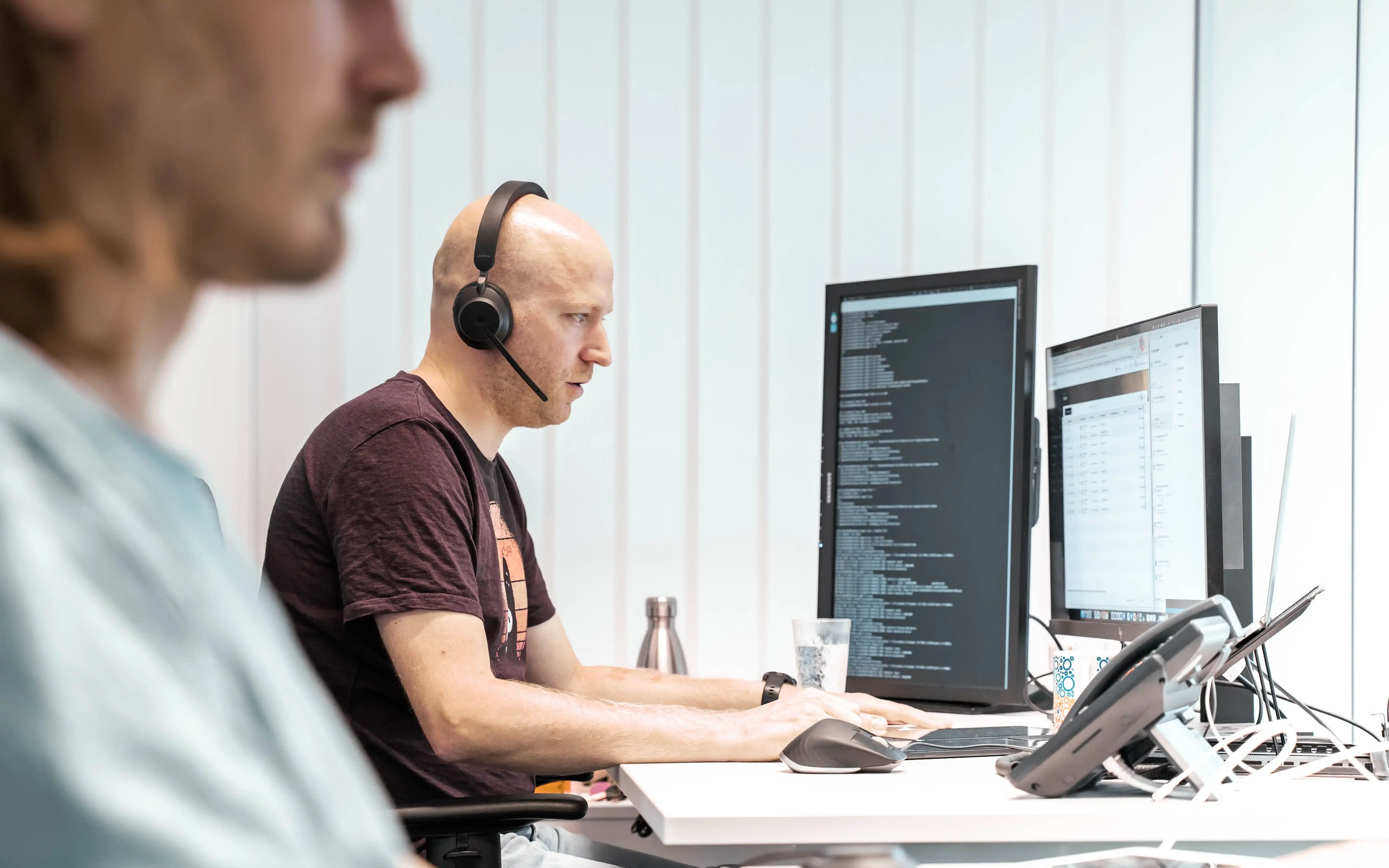 Relution Mitarbeiter Hanno Polomsky sitzt mit einem Headset vor zwei Bildschirmen und arbeitet konzentriert