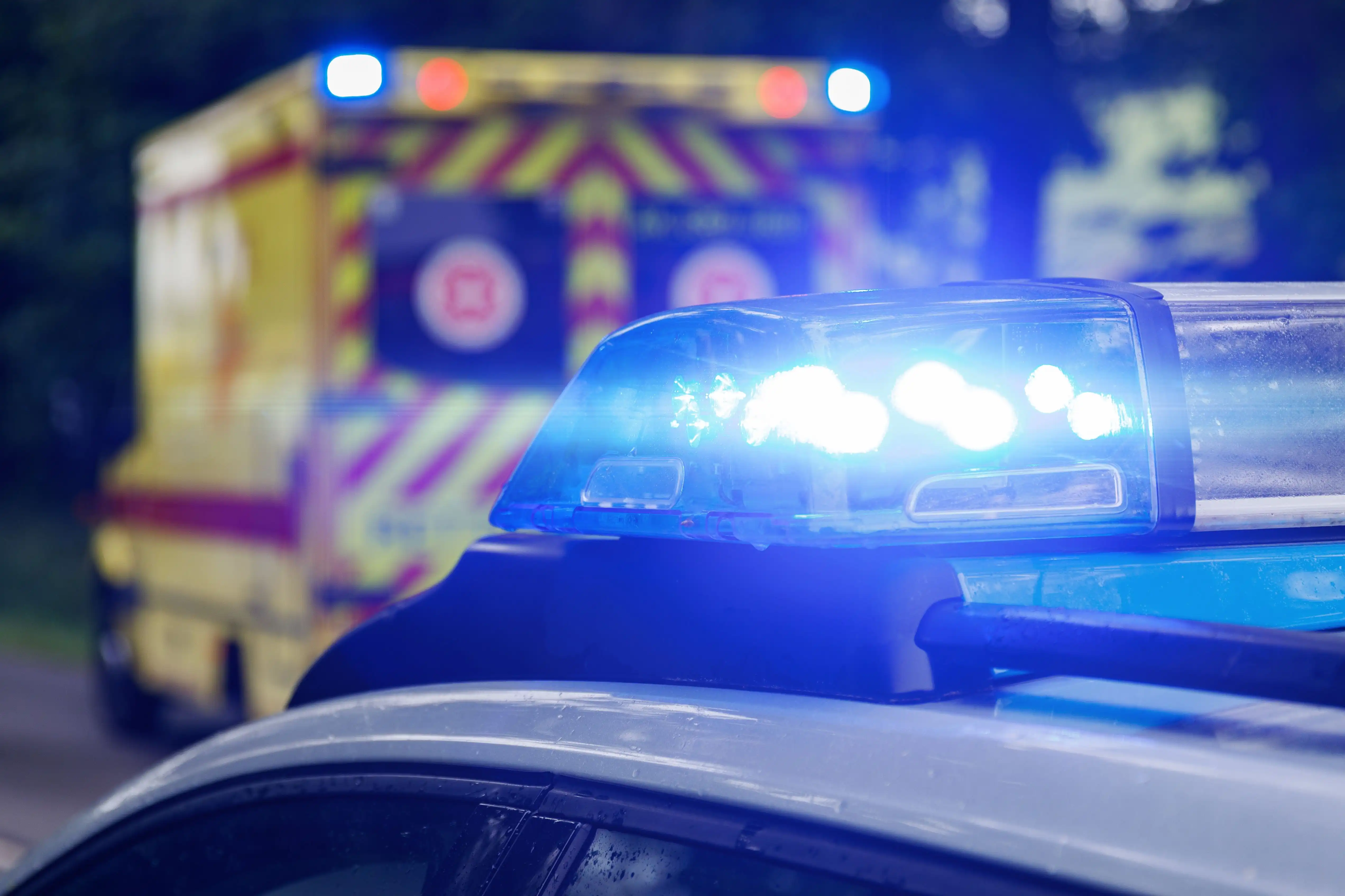 Nahaufnahme eines leuchtenden Blaulichts auf einem Fahrzeugdach, im unscharfen Hintergrund ein Rettungswagen.